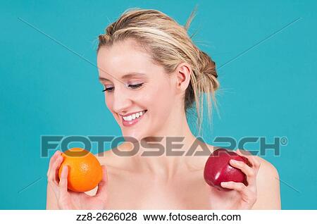 Stock Photo - Young Caucasian woman comparing apple and orange fruits. Fotosearch