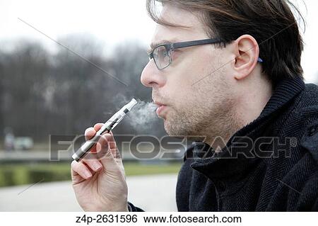 Young man smoking an e-cigarette View Large Photo Image Stock Photograph - Young man smoking an e-cigarette. Fotosearch