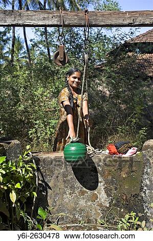Young woman draws water from well by hand with green pot on traditional rope pulley Mandrem village Goa India. View Large Photo Image Stock Photo - Young woman draws water from well by hand with green pot on traditional rope pulley Mandrem village Goa India.. Fotosearch