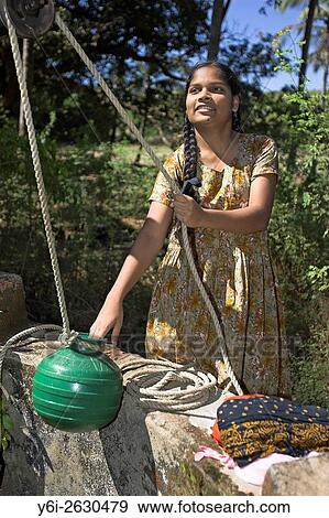 Young woman draws water from well by hand with green pot on traditional rope pulley Mandrem village Goa India. View Large Photo Image Stock Photo - Young woman draws water from well by hand with green pot on traditional rope pulley Mandrem village Goa India.. Fotosearch