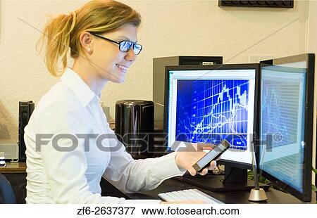 Young woman working at home office using cell phone and two computer monitors doing business with clients on the internet MR Model released. View Large Photo Image Stock Photo - Young woman working at home office using cell phone and two computer monitors doing business with clients on the internet MR Model released.. Fotosearch