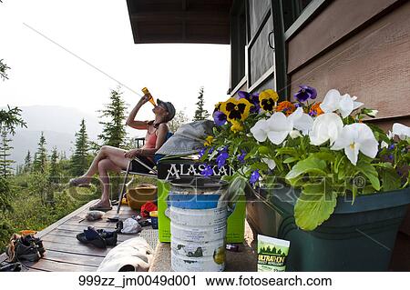 Woman Enjoys A Cold Beer On A Cabin Porch At Camp Denali Wonder