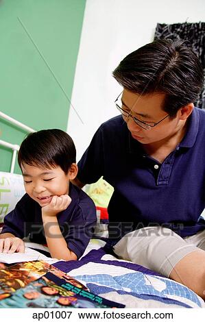 Boy lying on bed, hand on chin, reading a book, father next to him View Large Photo Image Stock Photo - Boy lying on bed, hand on chin, reading a book, father next to him. Fotosearch