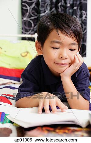 Boy lying on bed, hand on chin, reading a book View Large Photo Image Stock Photograph - Boy lying on bed, hand on chin, reading a book. Fotosearch