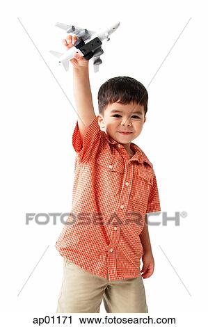 Stock Image - Boy standing and holding toy airplane, looking at camera. Fotosearch