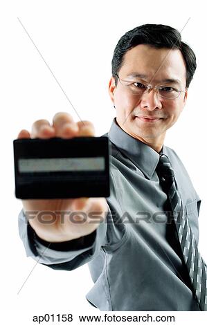 Stock Photo - Businessman holding credit card, looking at camera. Fotosearch