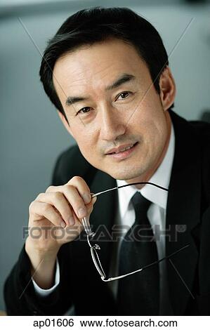 Stock Photograph - Businessman holding glasses, looking at camera, portrait. Fotosearch