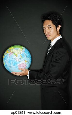 Stock Image - Businessman holding globe in hands, looking at camera. Fotosearch