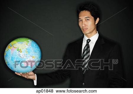 Stock Photo - Businessman holding globe in one hand, looking at camera. Fotosearch