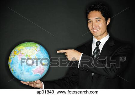 Businessman holding globe in one hand, pointing to it with the other View Large Photo Image Stock Photo - Businessman holding globe in one hand, pointing to it with the other. Fotosearch