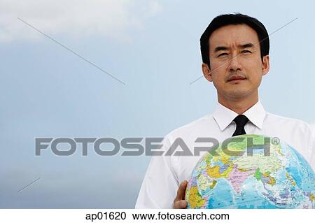 Stock Image - Businessman holding globe, looking away. Fotosearch
