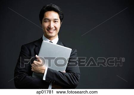 Stock Image - Businessman hugging laptop, looking at camera, smiling. Fotosearch