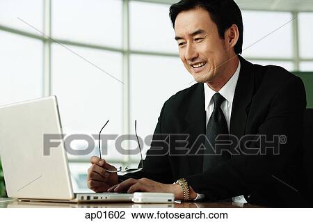 Stock Image - Businessman in office looking at laptop, smiling. Fotosearch