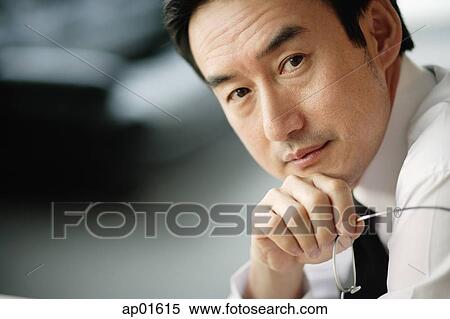 Stock Photography - Businessman looking at camera, hand on chin, head shot. Fotosearch