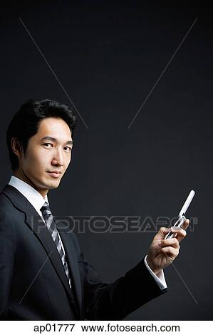 Stock Photo - Businessman looking at camera, holding mobile phone. Fotosearch