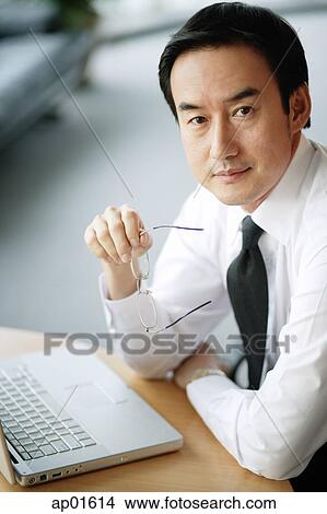 Businessman looking at camera, laptop open in front of him View Large Photo Image Picture - Businessman looking at camera, laptop open in front of him. Fotosearch
