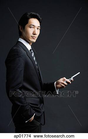 Businessman standing and holding mobile phone View Large Photo Image Picture - Businessman standing and holding mobile phone. Fotosearch