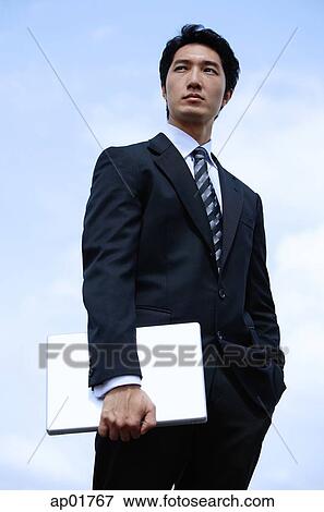 Stock Photo - Businessman standing, holding laptop. Fotosearch