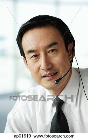 Stock Photo - Businessman using headset, looking at camera. Fotosearch