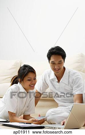 Couple at home in living room, looking at laptop View Large Photo Image Stock Image - Couple at home in living room, looking at laptop. Fotosearch