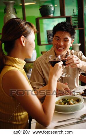 Stock Photo - Couple dining in Chinese restaurant, toasting with wine glasses. Fotosearch