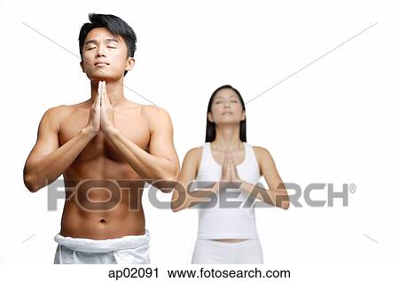 Stock Image - Couple doing yoga, hands together, man in front, woman standing behind him. Fotosearch