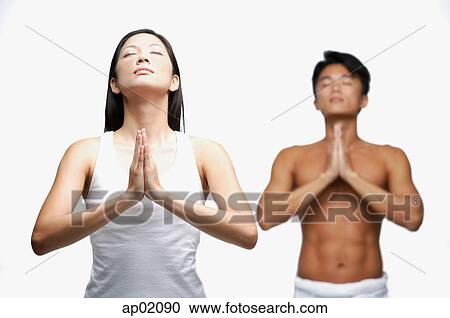 Stock Image - Couple doing yoga, woman in front, man standing in background. Fotosearch