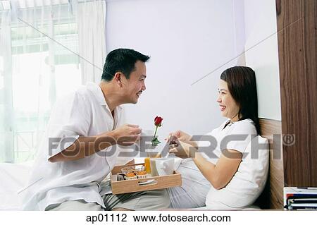 Stock Image - Couple in bedroom, breakfast tray between them. Fotosearch