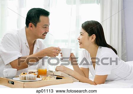 Stock Image - Couple in bedroom, having breakfast on bed. Fotosearch