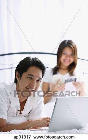 Couple in bedroom, man using laptop, smiling at camera View Large Photo Image Stock Photo - Couple in bedroom, man using laptop, smiling at camera. Fotosearch