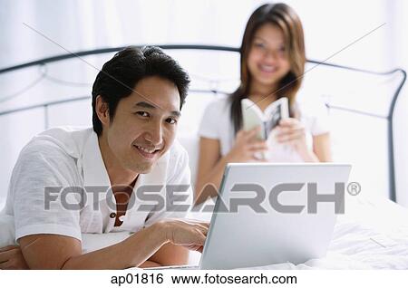Couple in bedroom, man using laptop, looking at camera View Large Photo Image Stock Photograph - Couple in bedroom, man using laptop, looking at camera. Fotosearch