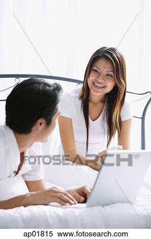 Couple in bedroom, woman smiling, man using laptop View Large Photo Image Stock Photography - Couple in bedroom, woman smiling, man using laptop. Fotosearch