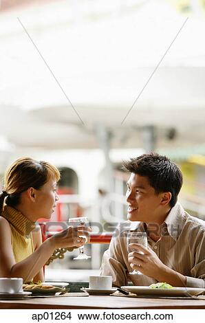 Picture - Couple in cafe, sitting side by side, holding glasses of water. Fotosearch
