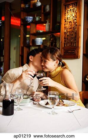 Stock Photo - Couple in Chinese restaurant, toasting with wine glasses, man kissing woman on cheek. Fotosearch
