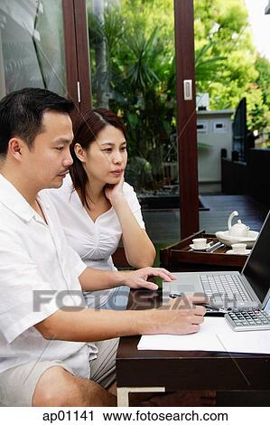 Couple in living room, looking at laptop View Large Photo Image Stock Image - Couple in living room, looking at laptop. Fotosearch