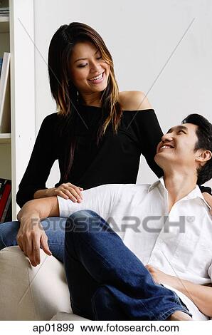 Stock Photo - Couple in living room, smiling at each other. Fotosearch