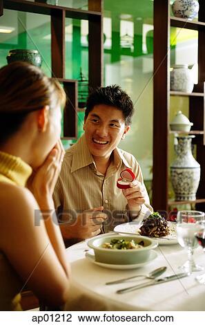 Stock Image - Couple in restaurant, man proposing with ring. Fotosearch