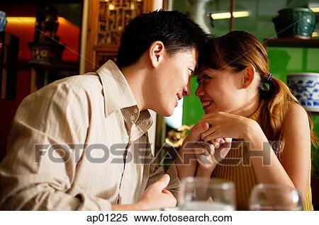 Stock Photography - Couple in restaurant, sitting face to face, man holding woman's hand. Fotosearch