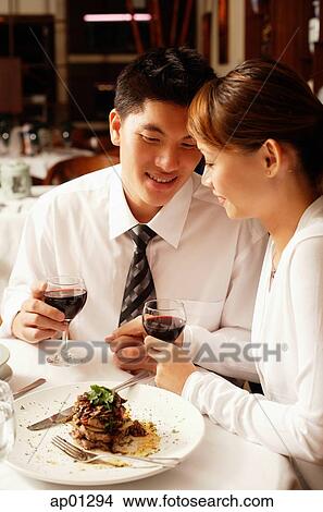Picture - Couple in restaurant, sitting side by side, holding hands. Fotosearch