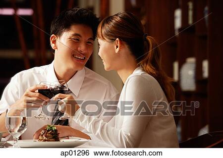 Stock Photograph - Couple in restaurant, sitting side by side, toasting with wine glasses. Fotosearch