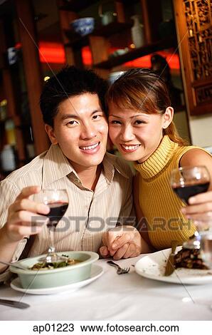 Stock Image - Couple in restaurant, smiling at camera, holding wine glasses. Fotosearch