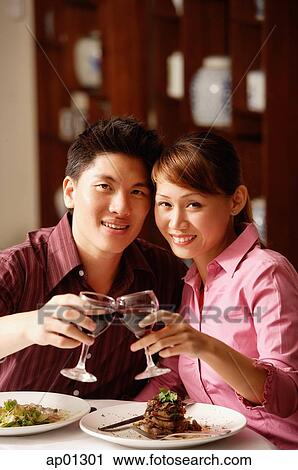 Couple in restaurant, toasting with wine glasses, looking at camera View Large Photo Image Stock Image - Couple in restaurant, toasting with wine glasses, looking at camera. Fotosearch