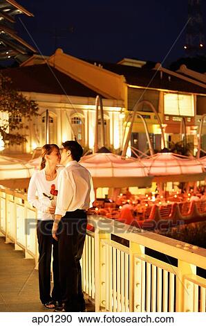Stock Image - Couple kissing on bridge, woman holding roses. Fotosearch
