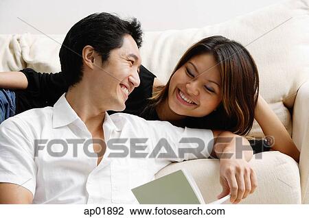 Stock Image - Couple looking at each other, man holding book. Fotosearch