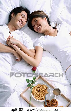 Couple lying on bed, holding hands, breakfast on tray next to them View Large Photo Image Stock Image - Couple lying on bed, holding hands, breakfast on tray next to them. Fotosearch