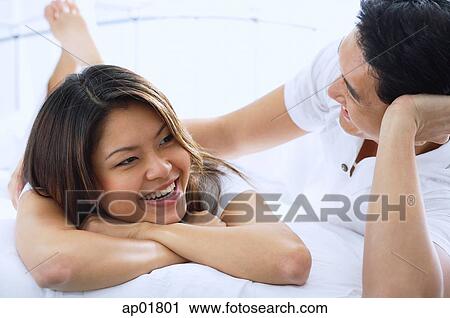Stock Image - Couple on bed, smiling. Fotosearch