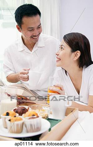 Couple on bed, with drinks, looking at each other, breakfast tray in front of them View Large Photo Image Picture - Couple on bed, with drinks, looking at each other, breakfast tray in front of them. Fotosearch
