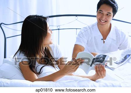Stock Image - Couple on bed, woman turning to show man book. Fotosearch