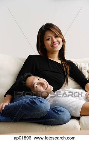 Couple on sofa, man lying on womans lap, both smiling at camera View Large Photo Image Stock Photograph - Couple on sofa, man lying on womans lap, both smiling at camera. Fotosearch