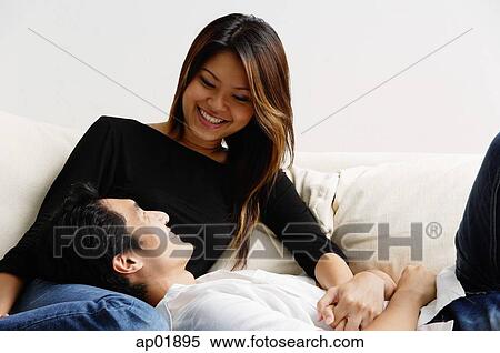 Stock Photography - Couple on sofa, man lying on womans lap, smiling at her. Fotosearch